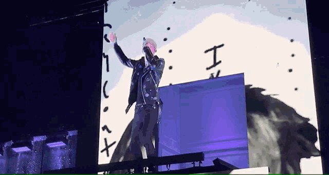 a man stands on a stage in front of a large screen with the letter i on it