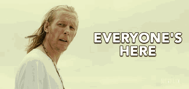 a man with long hair is standing in front of a sign that says " everyone 's here "