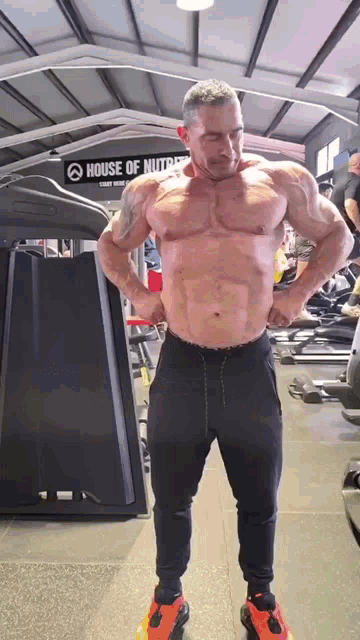 a man is standing in a gym with his hands on his hips and a sign that says house of nutrition .