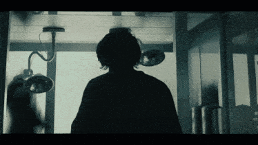 a silhouette of a person in an operating room with lights hanging from the ceiling