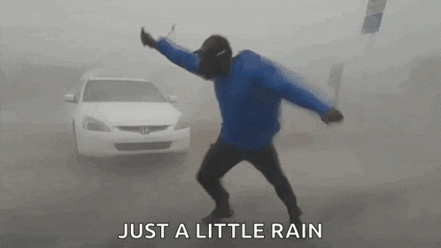 a man in a blue jacket is dancing in the rain in front of a white car .
