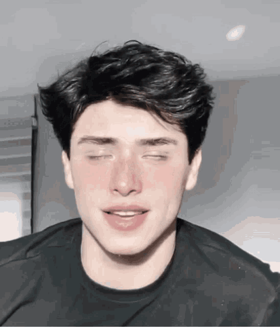 a young man with his eyes closed is wearing a black t-shirt .