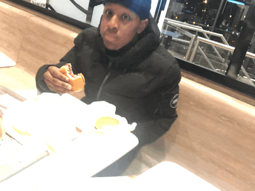 a man in a black jacket is eating a hamburger with a sticker on the wall that says ' enjoy your '