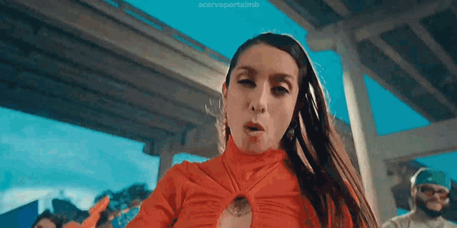 a woman in a red top is standing under a bridge making a funny face .