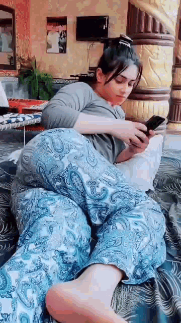 a woman is sitting on a bed with her legs crossed and looking at her phone .
