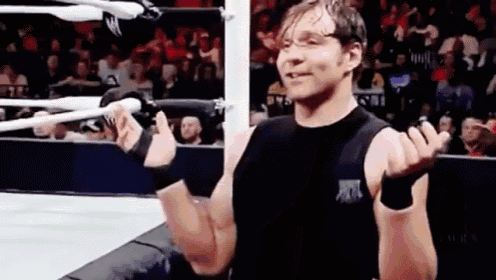 a wrestler in a black tank top is standing in a wrestling ring .