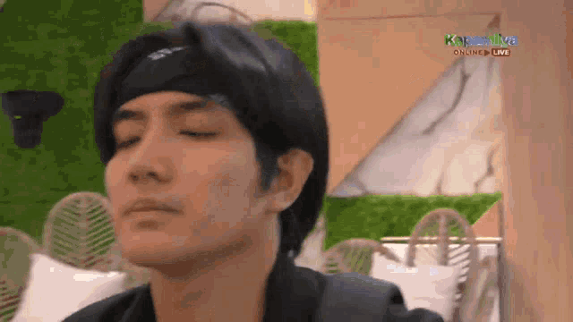 a man wearing a headband is sitting with his eyes closed in front of a sign that says kapamilya online live