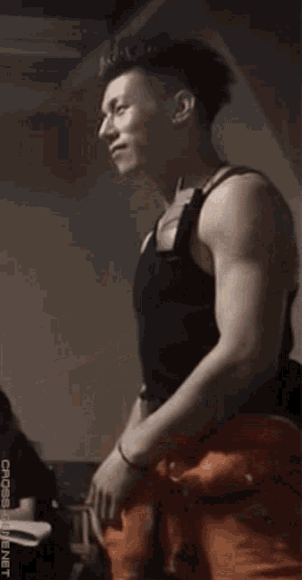 a man in a black tank top and orange pants is standing in a dark room .