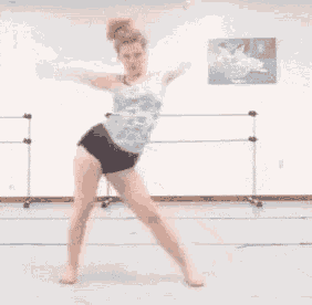 a woman in a tank top and black shorts is dancing in a dance studio .