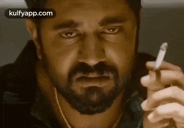 a man with a beard is holding a cigarette in his hand .