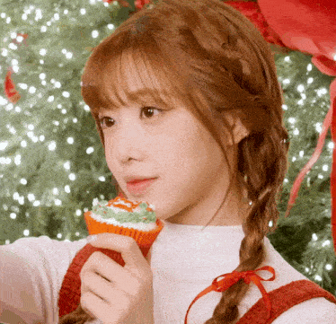 a girl with braids is holding a cupcake with a christmas tree on it