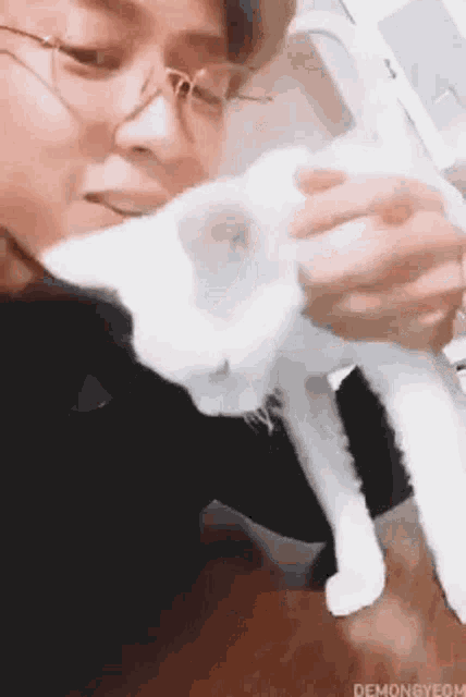 a man wearing glasses is holding a white cat .