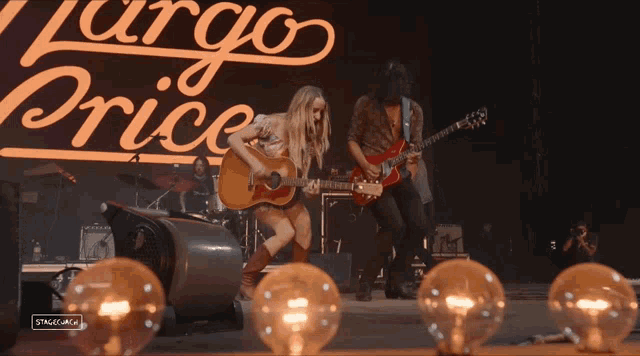 a woman playing an acoustic guitar and a man playing a red electric guitar in front of a sign that says argo price