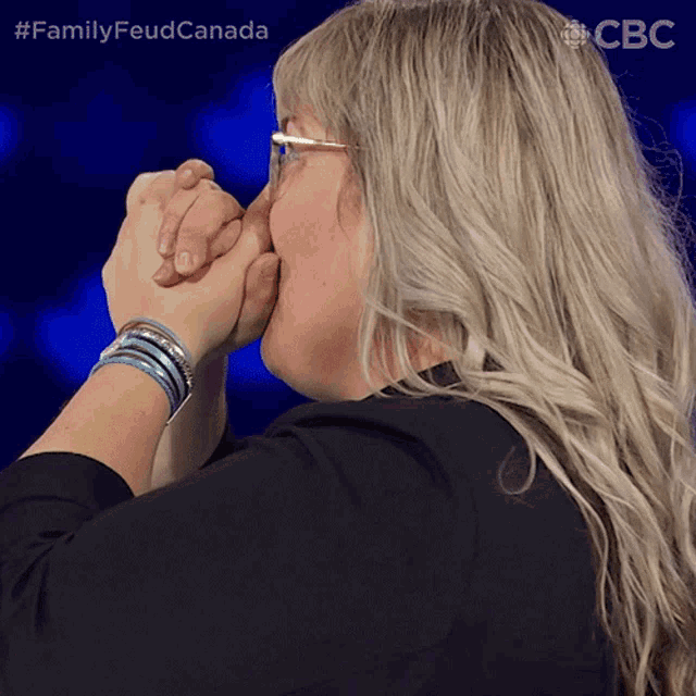 a woman holds her hands together with the hashtag familyfeud canada on the bottom