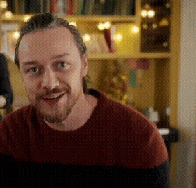 a man with a beard wearing a red and black sweater smiles