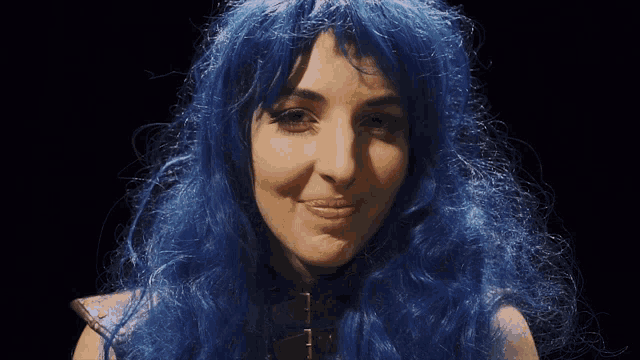 a woman wearing a blue wig and a choker looks at the camera