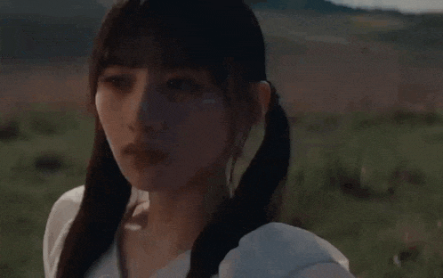 a woman with pigtails is standing in a field with mountains in the background