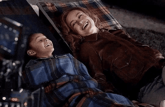 a woman and a child are laying in a hammock with blankets .