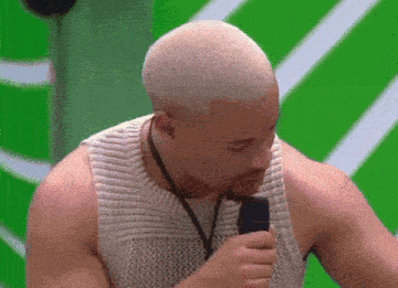 a man in a white tank top is holding a microphone in his mouth .