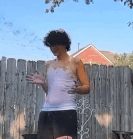 a woman in a white tank top is standing in front of a wooden fence
