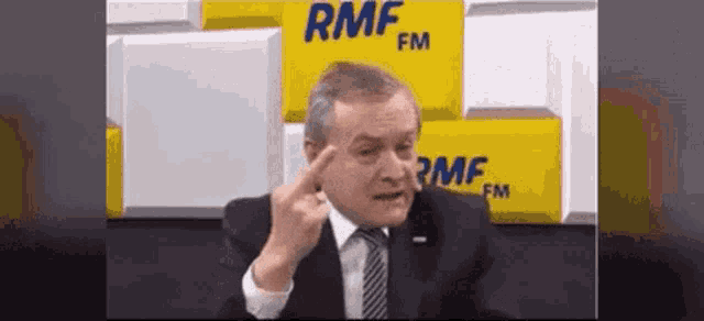 a man in a suit and tie is making a funny face in front of a sign that says rmf fm