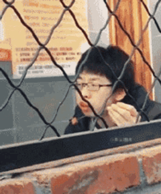 a man with glasses is behind a chain link fence eating food