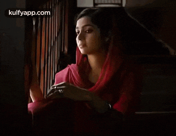 a woman in a red scarf is sitting on a set of stairs looking out the window .