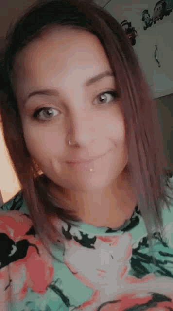 a woman with a nose ring and a floral shirt is smiling for the camera .