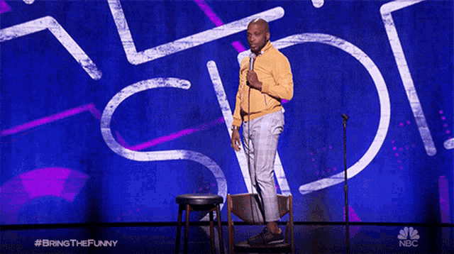 a man stands on a stool in front of a sign that says " bring the funny "