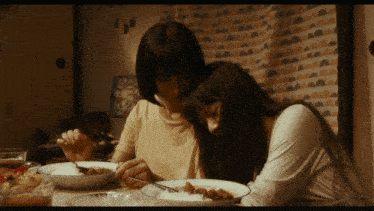 two women are sitting at a table eating a bowl of food