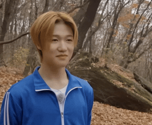 a young man wearing a blue jacket is standing in the woods
