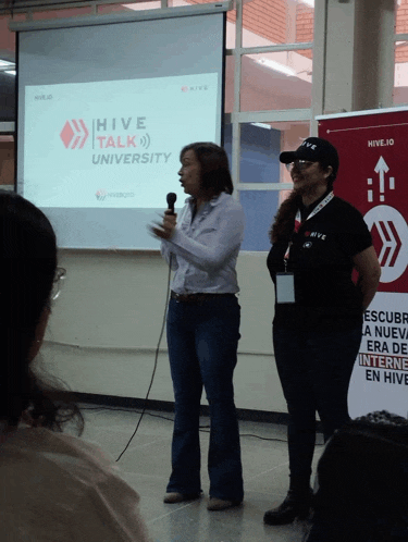 two women standing in front of a hive talk university projector screen