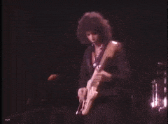 a man is playing a guitar on a stage in a dark room