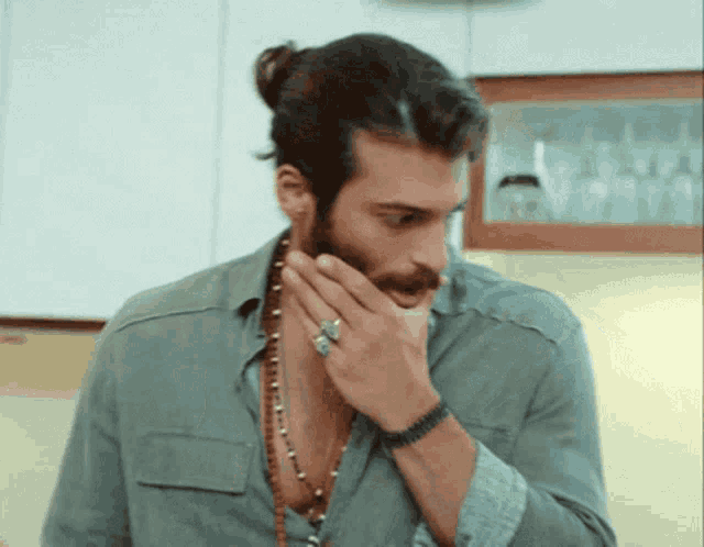 a man with long hair and a beard wearing a necklace and a ring on his finger