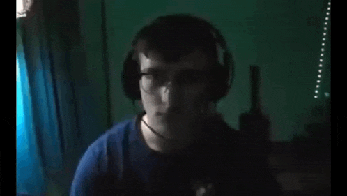 a man wearing glasses and a blue shirt is standing in a dark room looking at the camera .