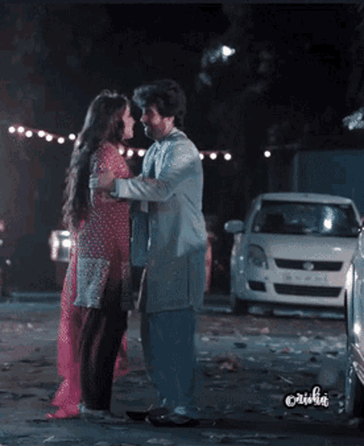 a man and a woman are hugging in a parking lot with a car in the background