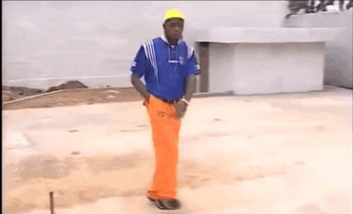 a man in a blue shirt and orange pants is standing on a concrete surface