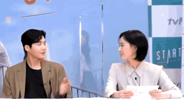 a man and a woman are sitting at a table in front of a sign that says start .