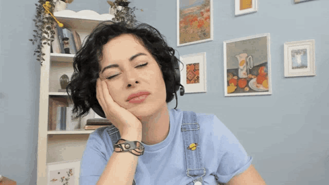a woman wearing a blue shirt and overalls holds her hand to her face