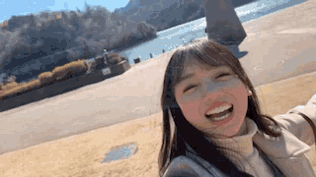 a woman is taking a selfie in front of a lake while smiling .