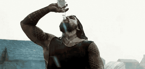 a man is drinking water from a bottle while standing in front of a building .