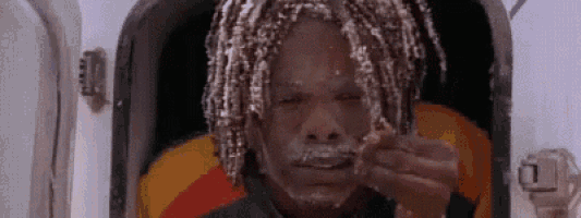 a man with dreadlocks and a beard is sitting in a chair with a piece of food in his mouth .
