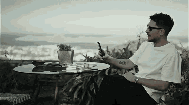 a man with a tattoo on his arm is sitting at a table holding a cell phone