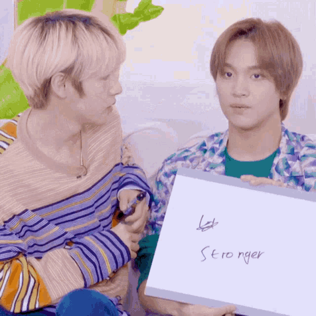 two young men are sitting next to each other and one of them is holding a sign that says let 's be stronger