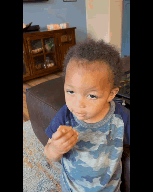 a young boy wearing a blue camo shirt is eating something