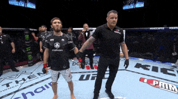a man in a ufc shirt stands in a ring with a referee