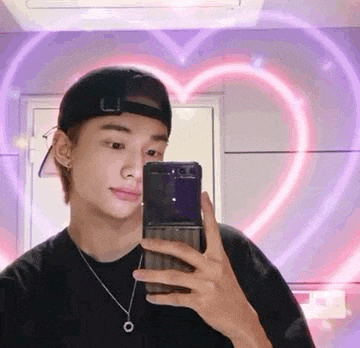 a young man is taking a selfie with his phone in front of a heart .