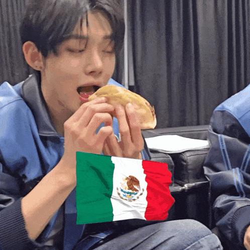a person is eating a taco with a mexican flag behind them