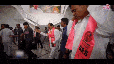 a man wearing a pink shirt that says brs stands in a crowd