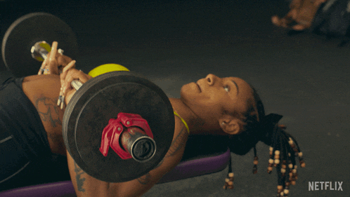 a woman in a yellow top is lifting a dumbbell with a netflix logo in the corner